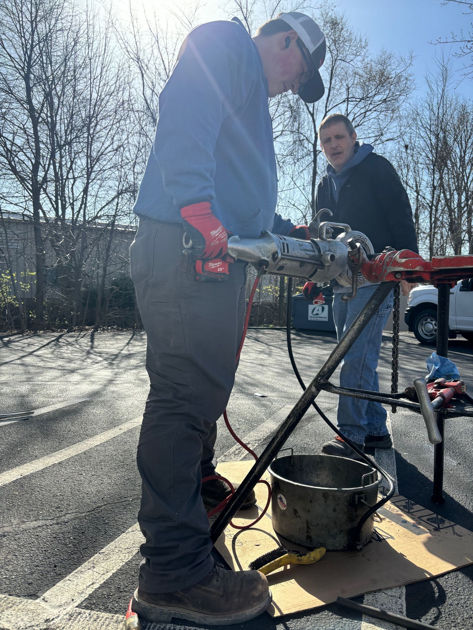 Two men are working on a pipe in a parking lot.