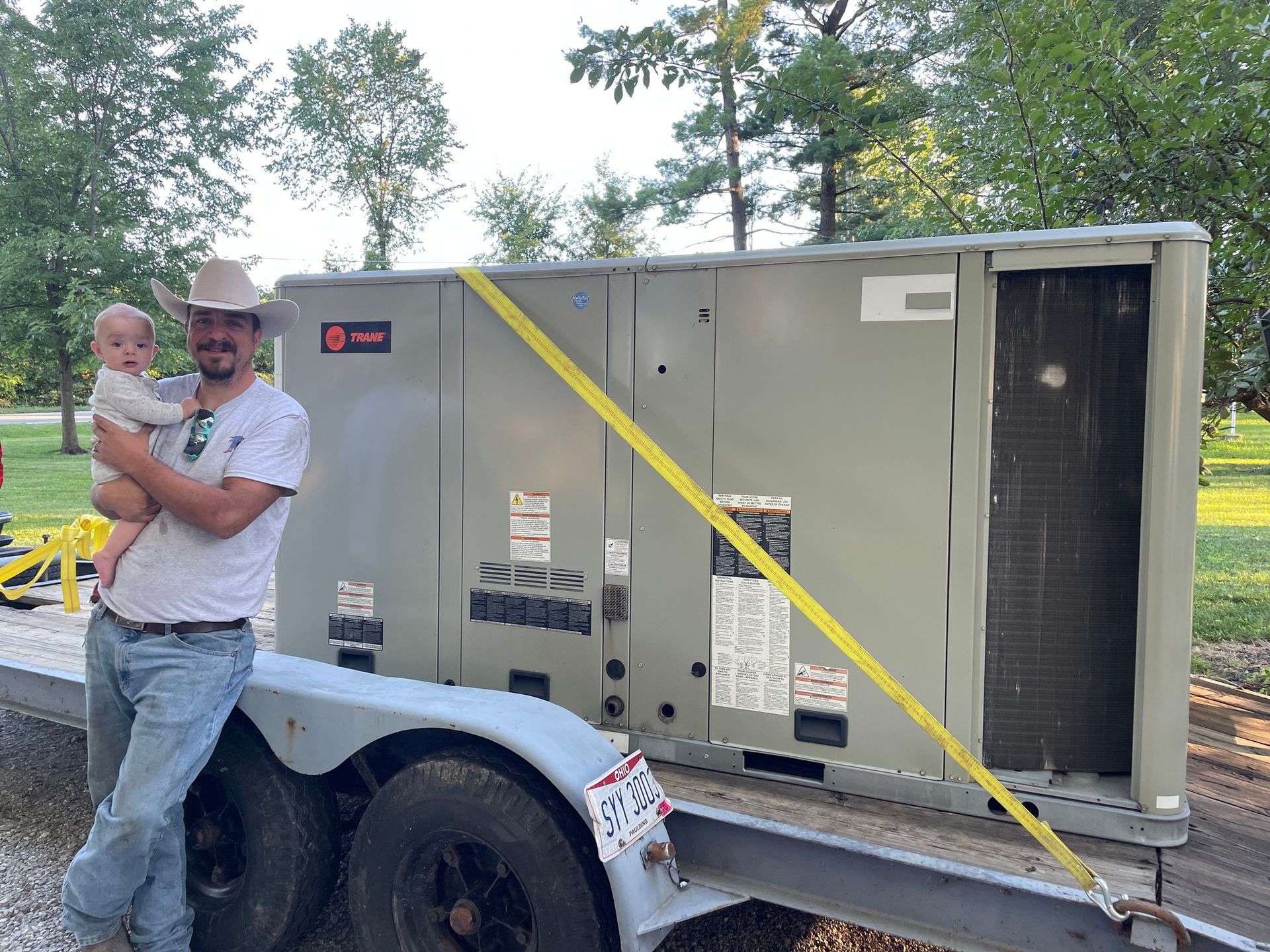 A man is holding a baby while standing next to a trailer.