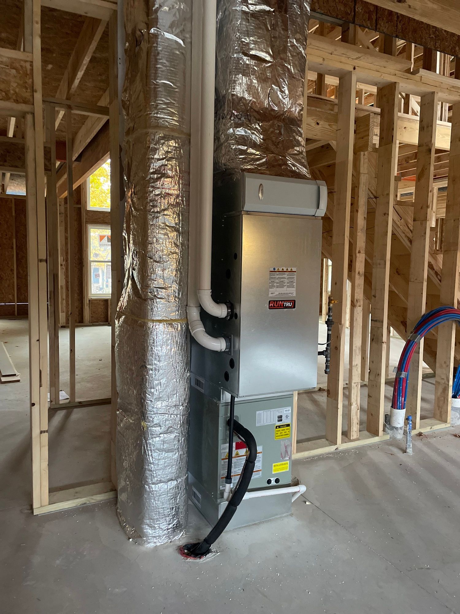 An air conditioner is sitting in the middle of a room in a house under construction.