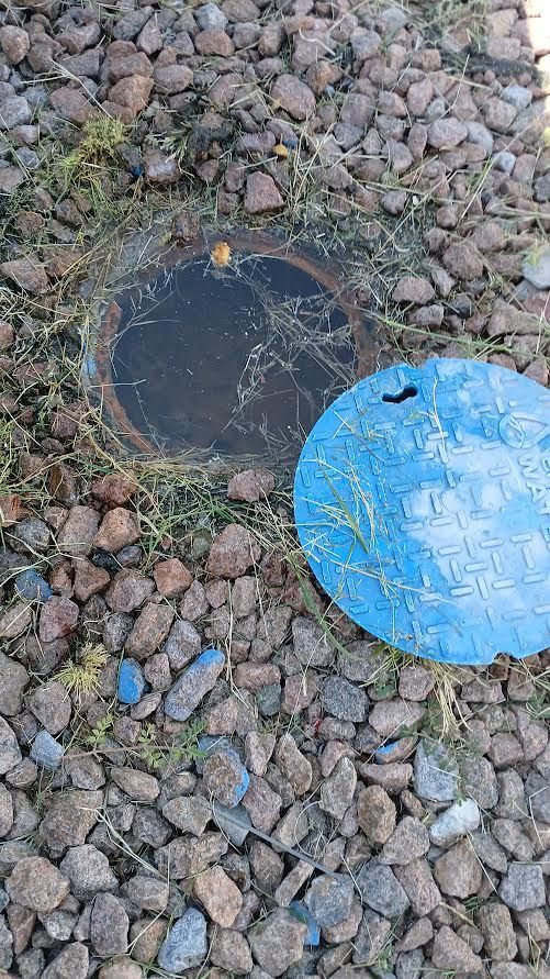 Two circular utility covers in gravel, one black and one bright blue.