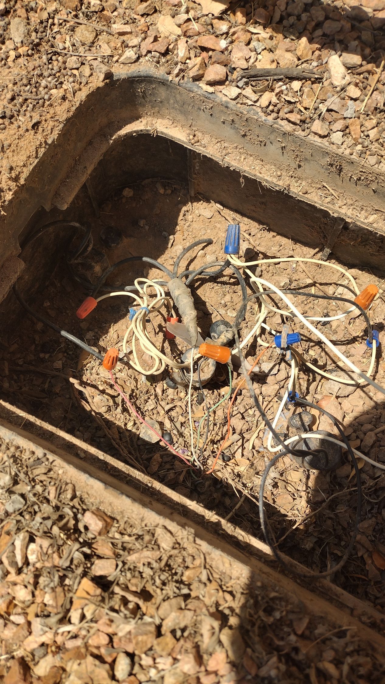 Open utility box with tangled cables and connectors in a gravel ground area