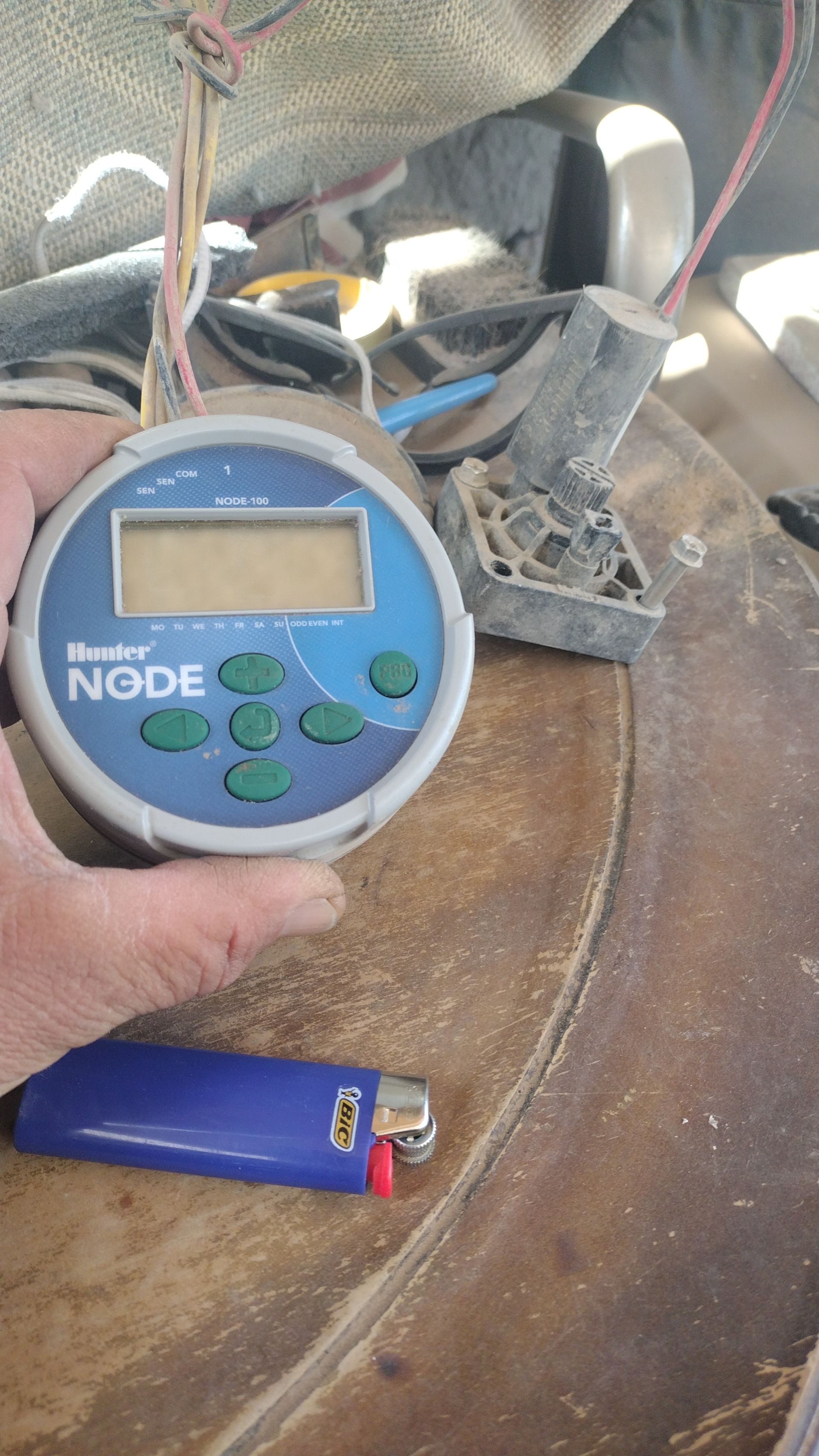 Handheld blue digital device on a rusted metal surface, with wires and tubing in the background
