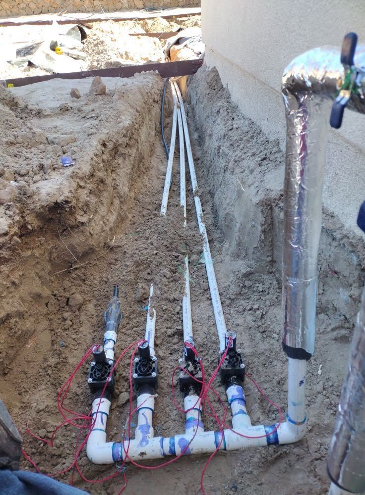 Underground plumbing lines and valves installed in a trench beside a building wall.