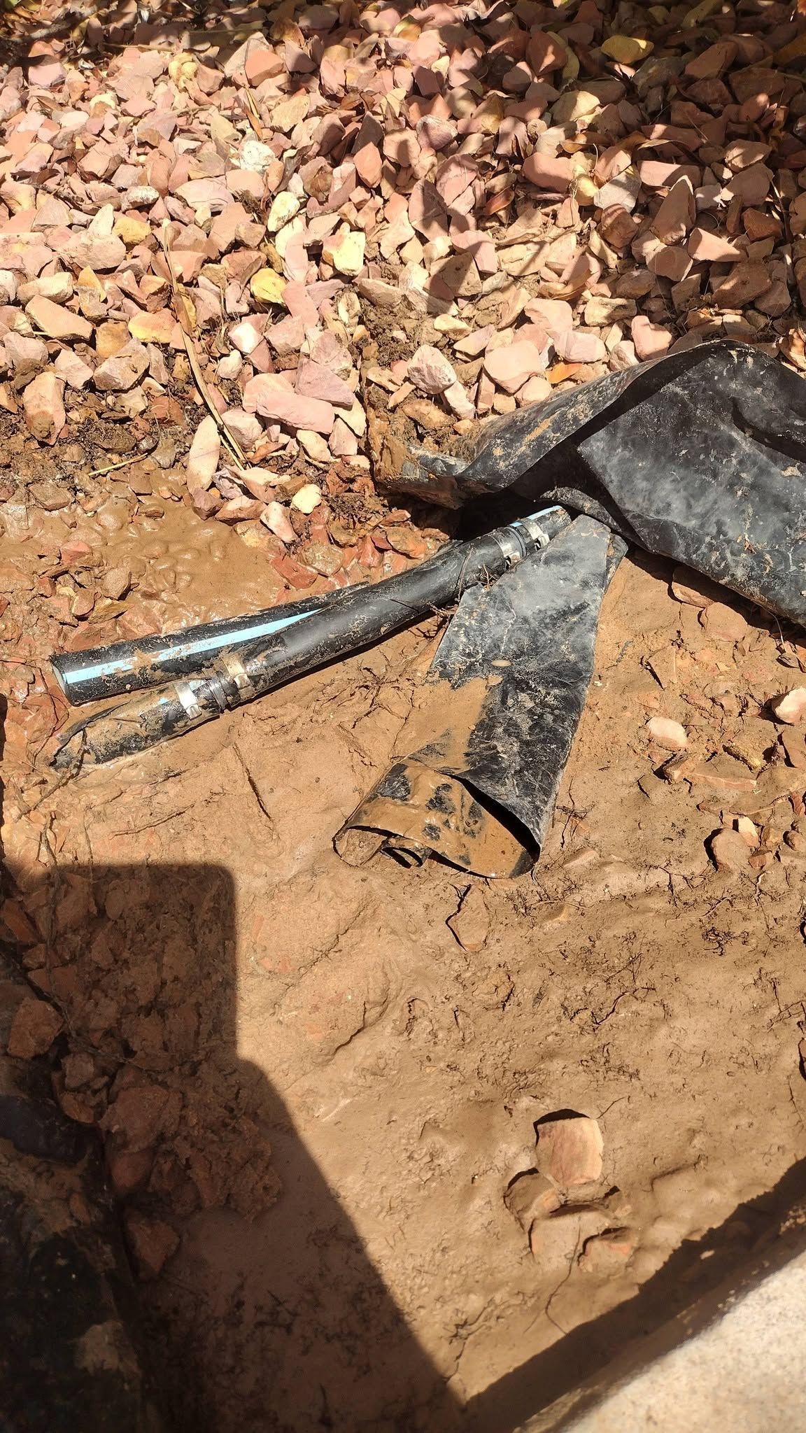 Black cable and metal fitting partly buried in dirt and gravel.