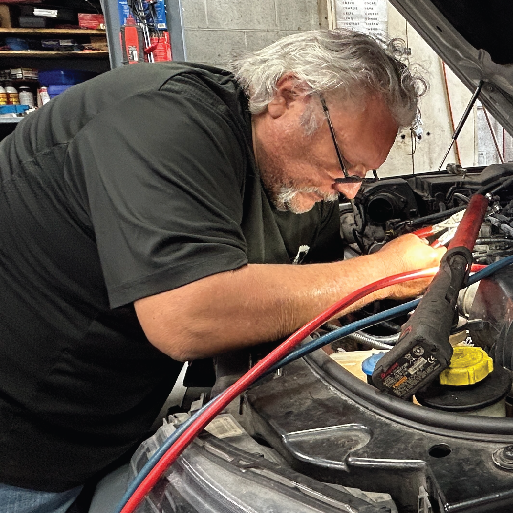 Mechanic working on a car engine, using tools. Gray-haired man in a garage.