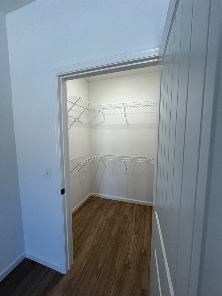 Open closet with wire shelves and wood flooring in a white room