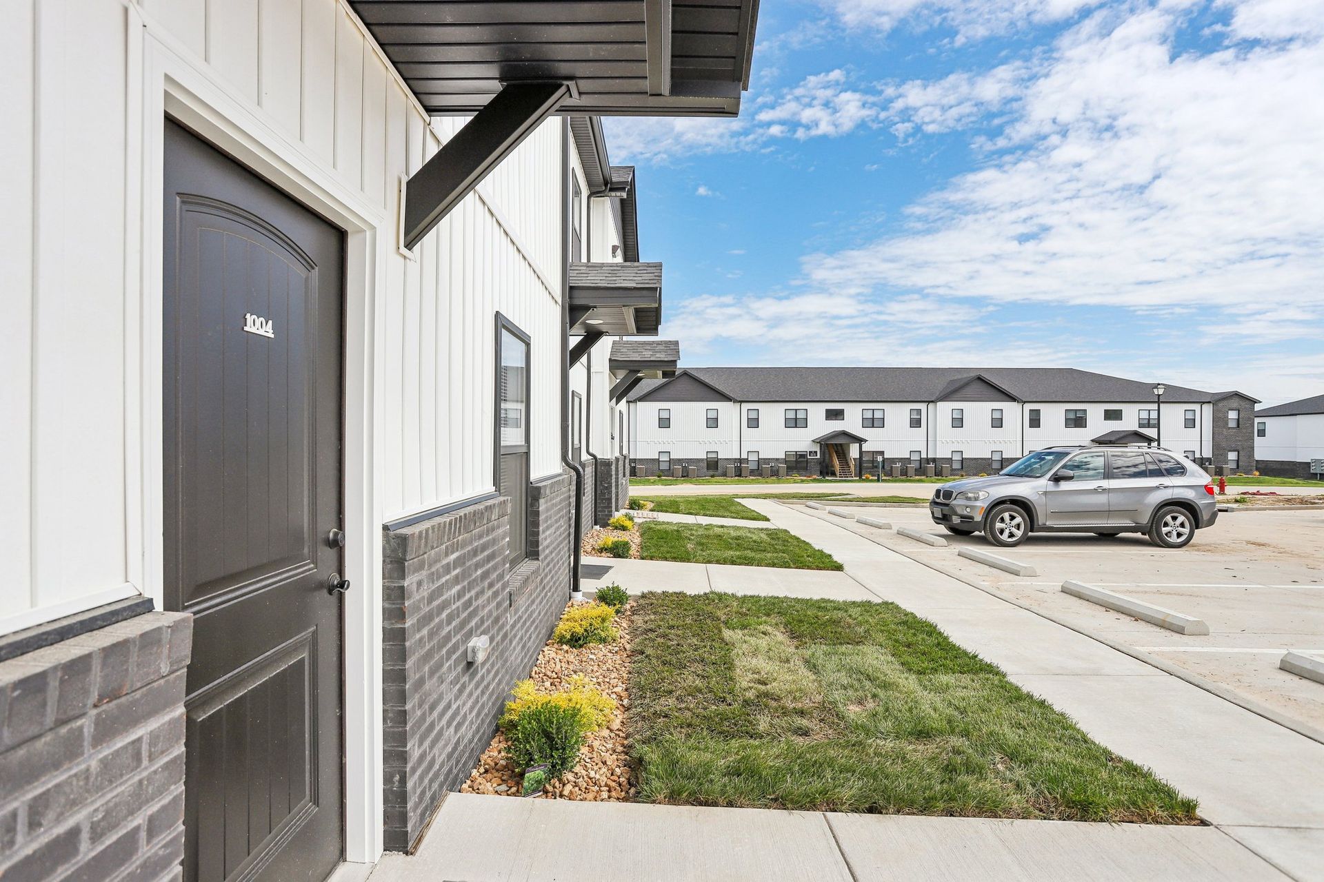 Apartment building exterior with sidewalk, small lawn, and parked car in a residential lot
