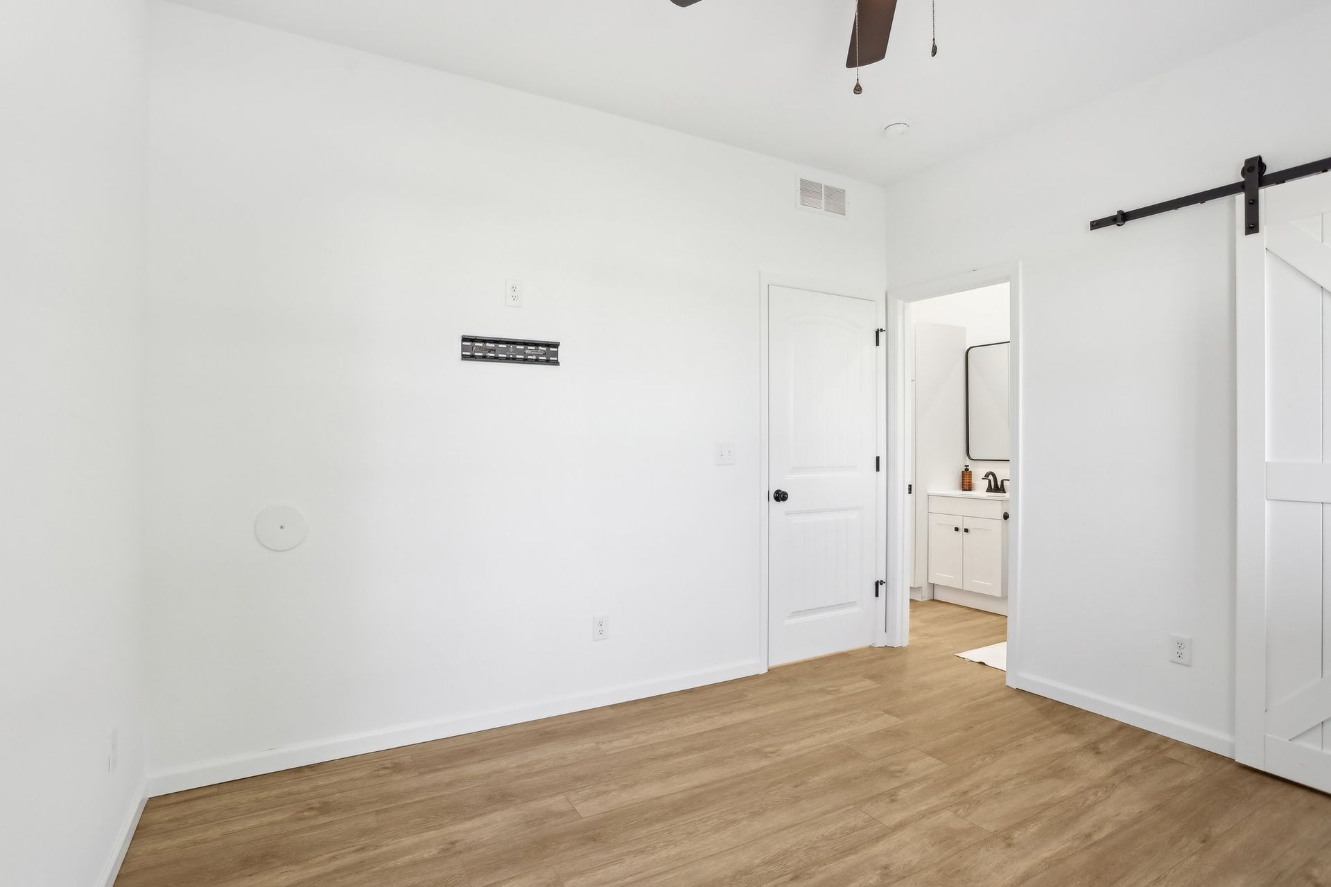 Empty white bedroom with wood floors and an open door to a bathroom