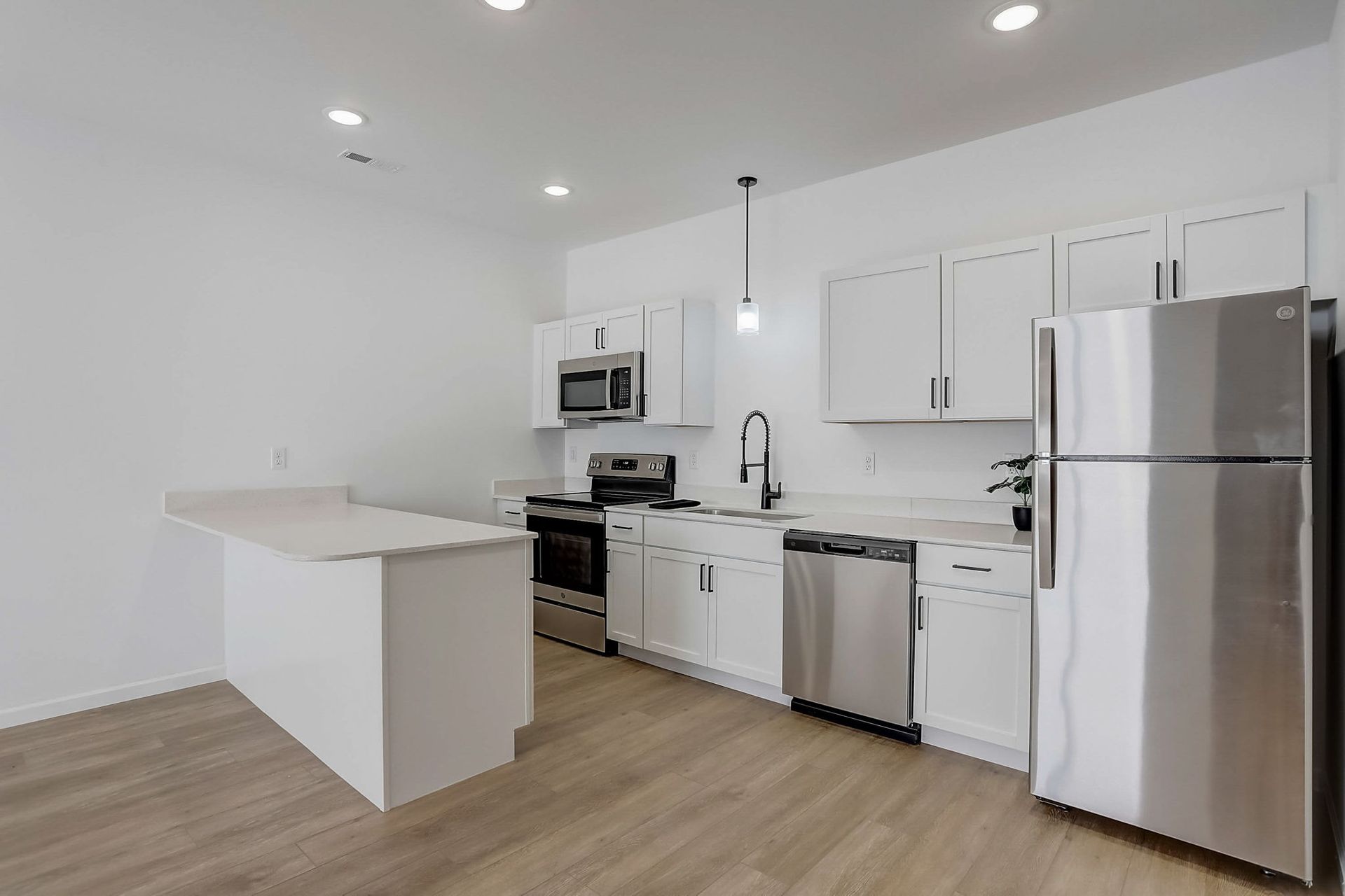 Bright white modern kitchen with stainless steel appliances, island, and wood floors