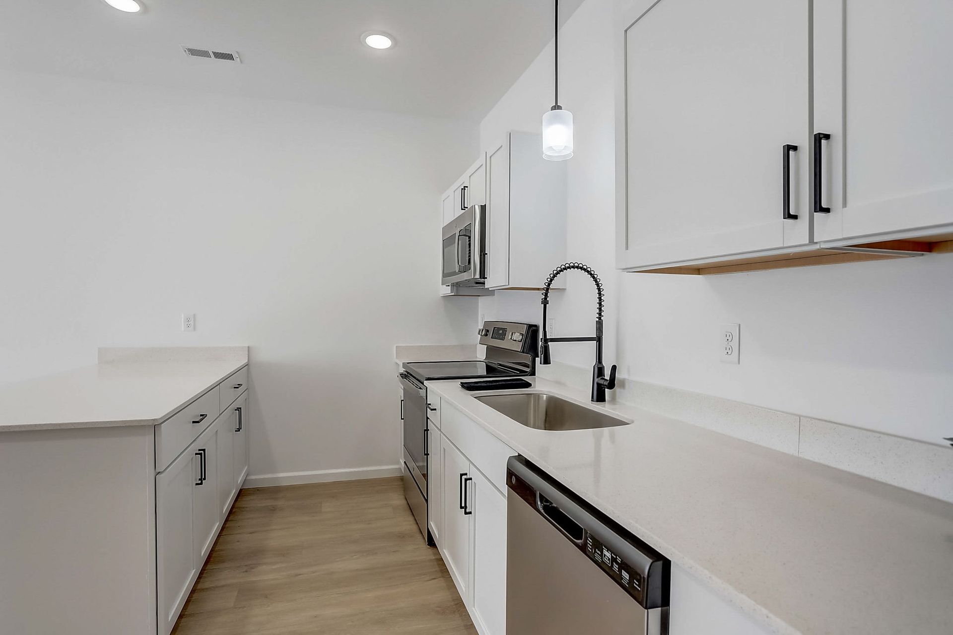 Modern white kitchen with island, pendant light, stainless appliances, and light wood flooring