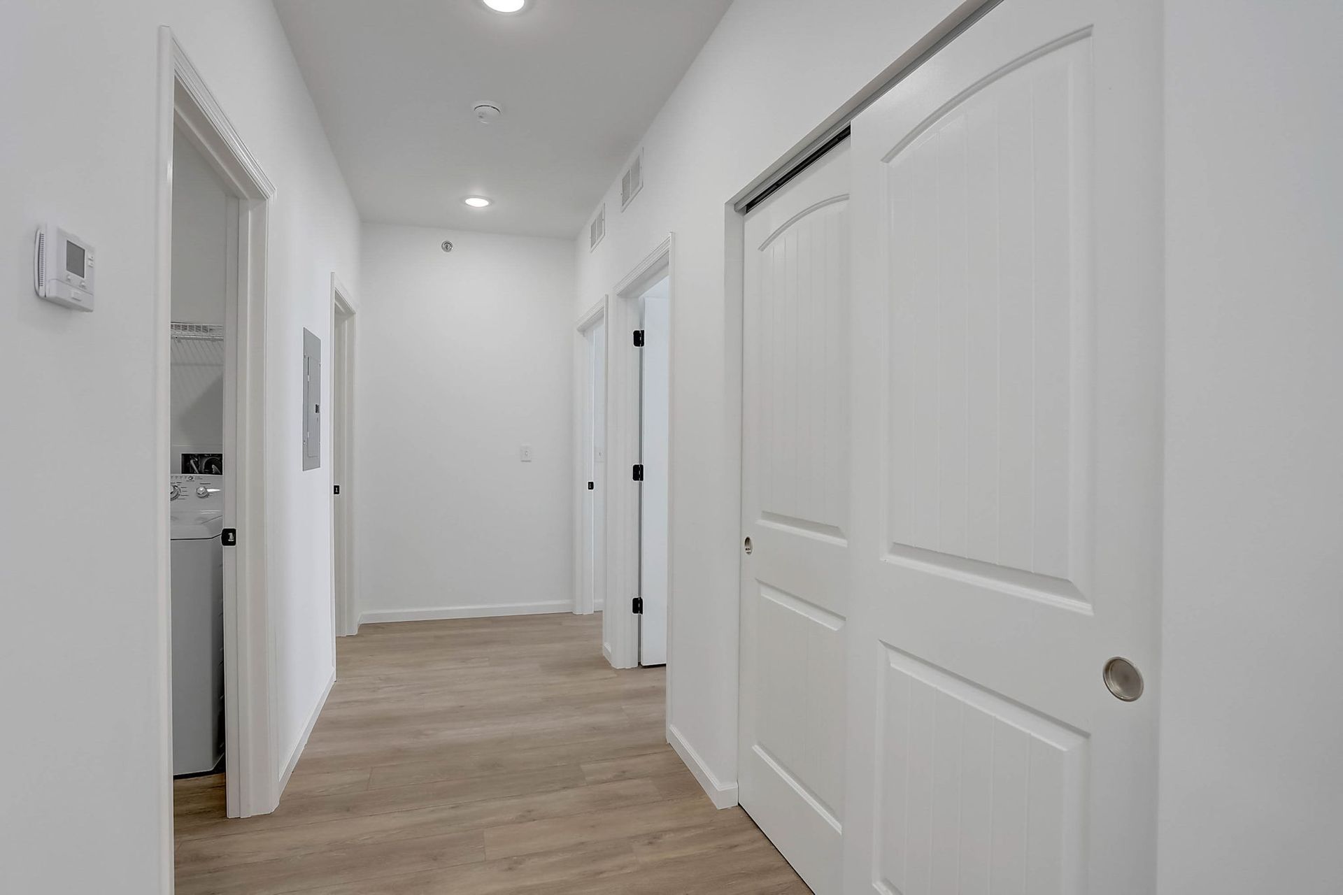 Bright hallway with white doors and light wood flooring, viewed from one end of the corridor.