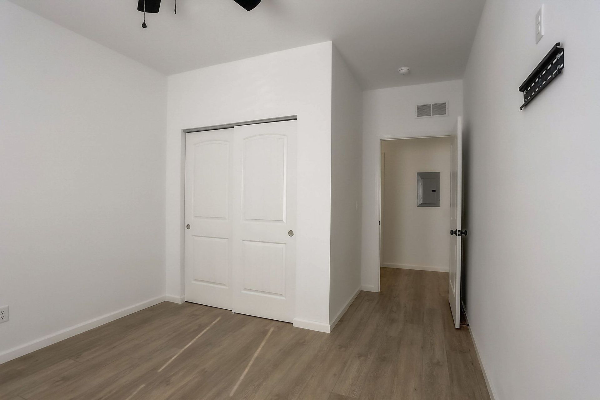 Empty white bedroom with wood flooring, closet doors, and a hallway entrance