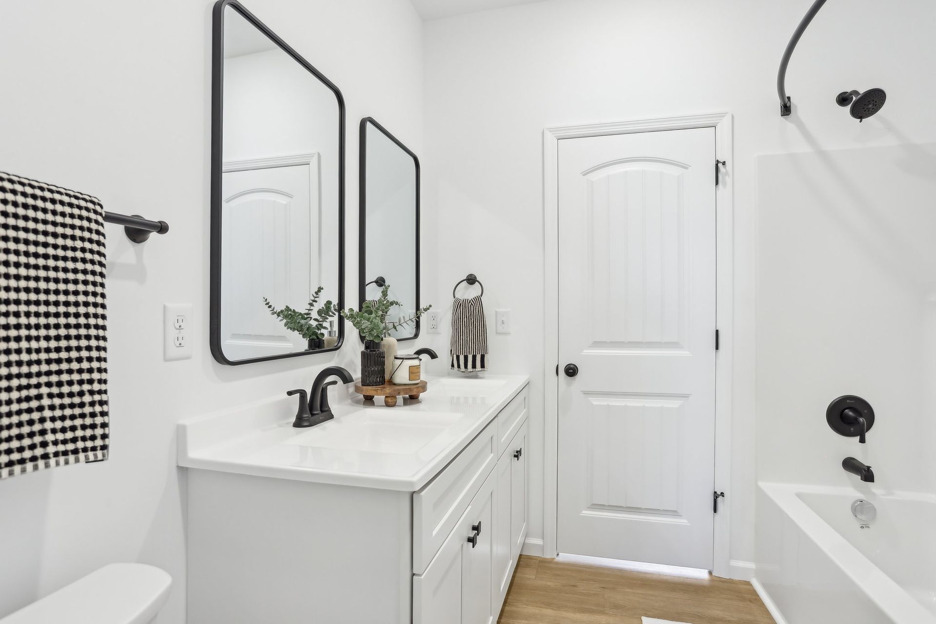 Bright white bathroom with vanity, double mirrors, bathtub, and white door.
