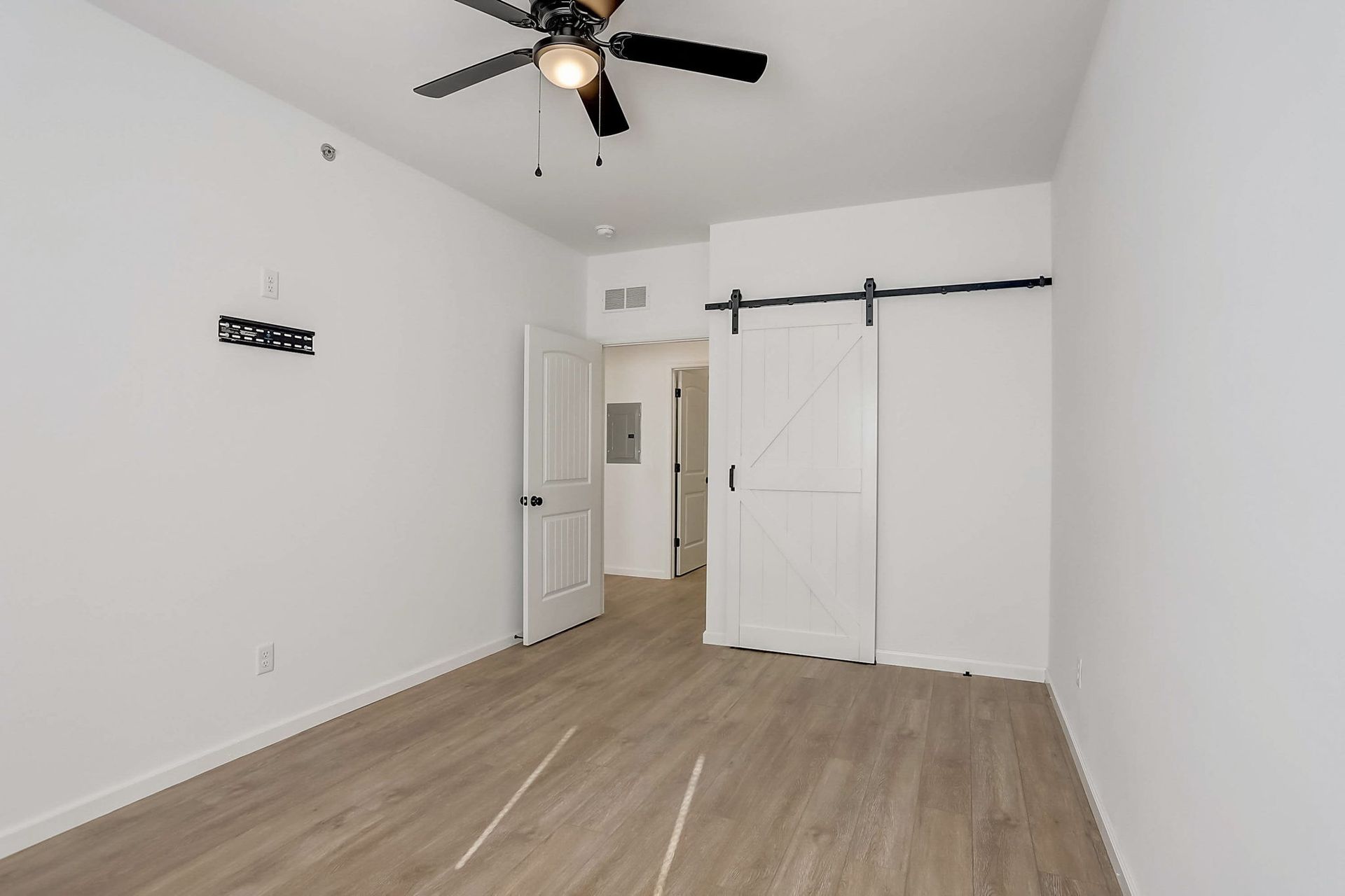 Empty white bedroom with wood-look floor, ceiling fan, sliding closet doors, and open doorway.
