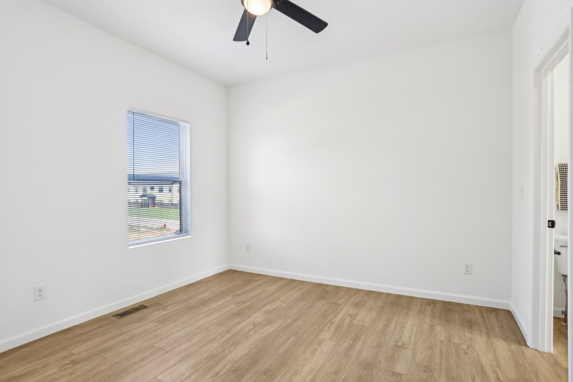 Empty white bedroom with wood flooring, a window, and a ceiling fan.