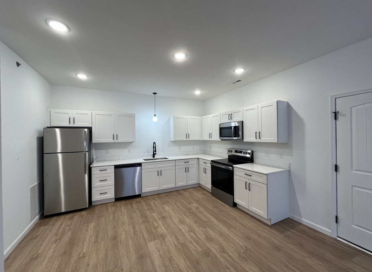 Bright modern white kitchen with stainless steel appliances, wood flooring, and recessed ceiling lights