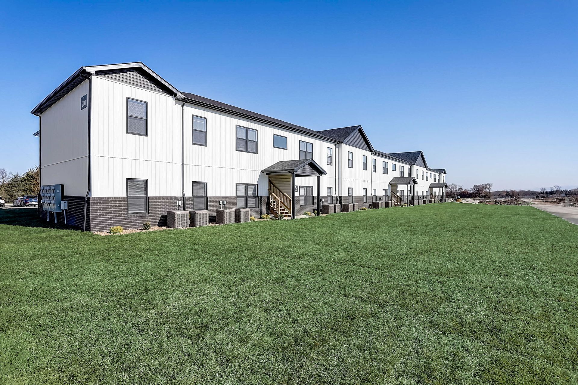 Long white apartment building beside a wide green lawn under a clear blue sky