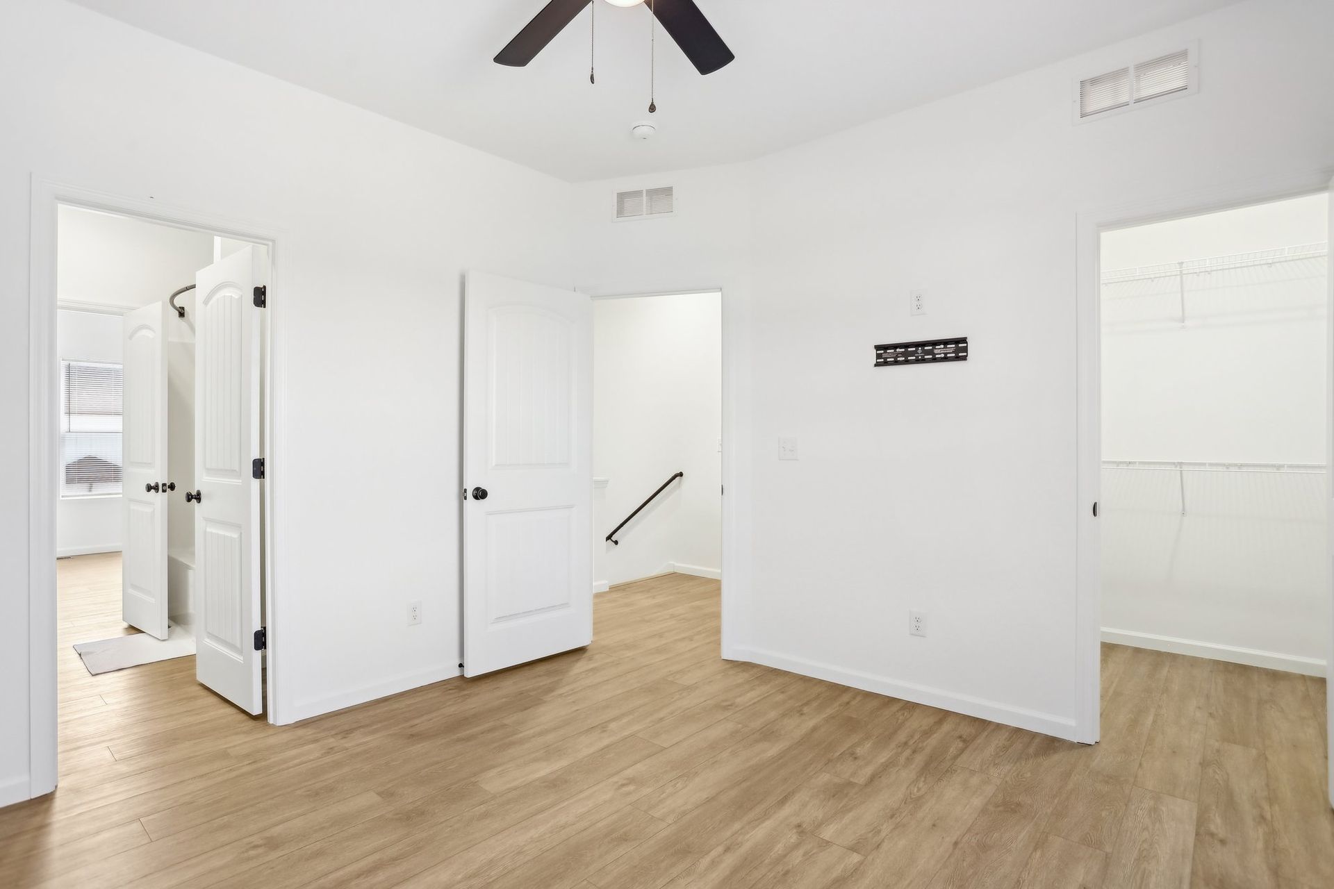 Bright empty white room with wood floors, ceiling fan, and open doorways to adjoining spaces