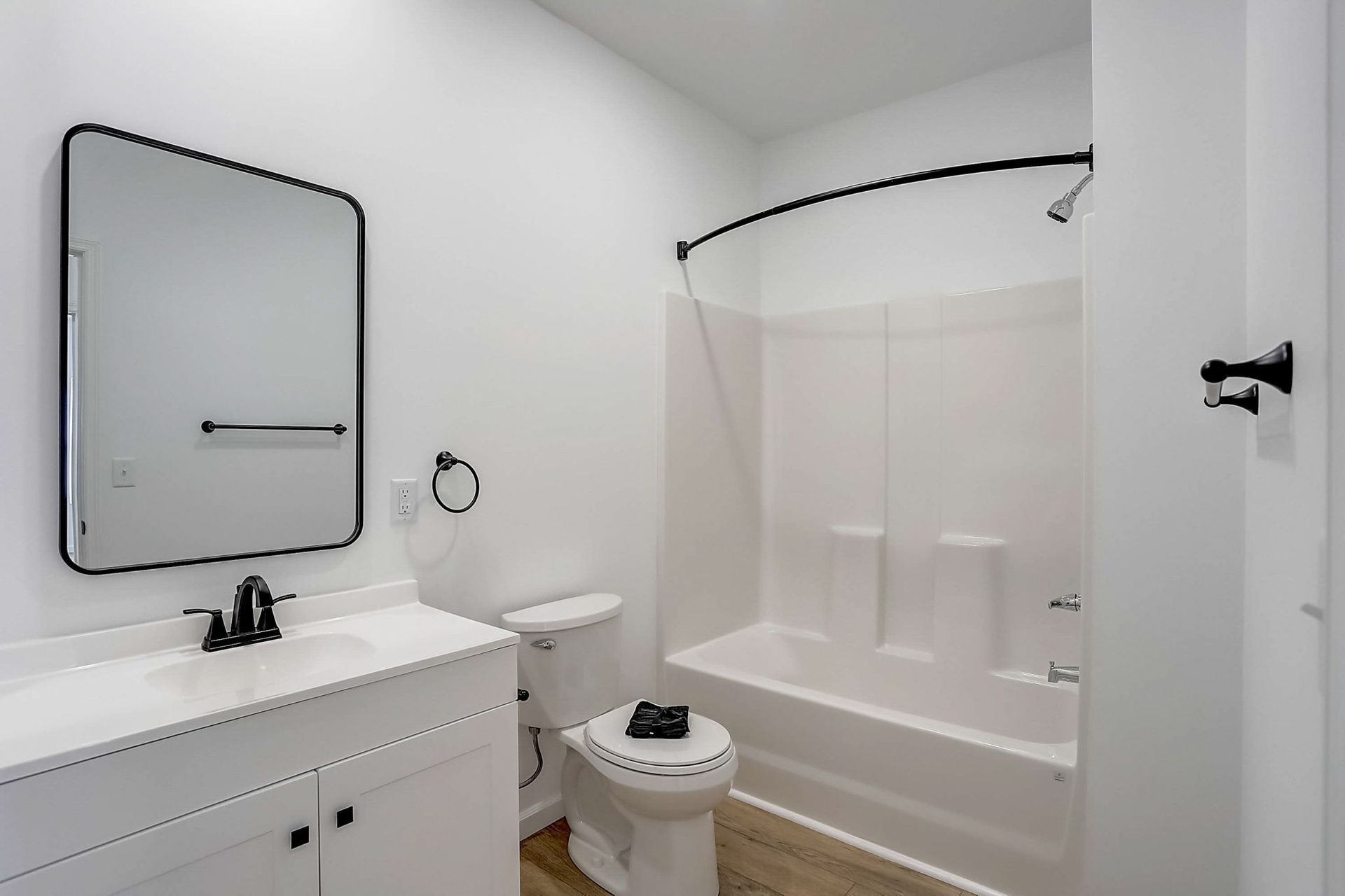Bright bathroom with white vanity, toilet, and tub-shower combo with black curtain rod.