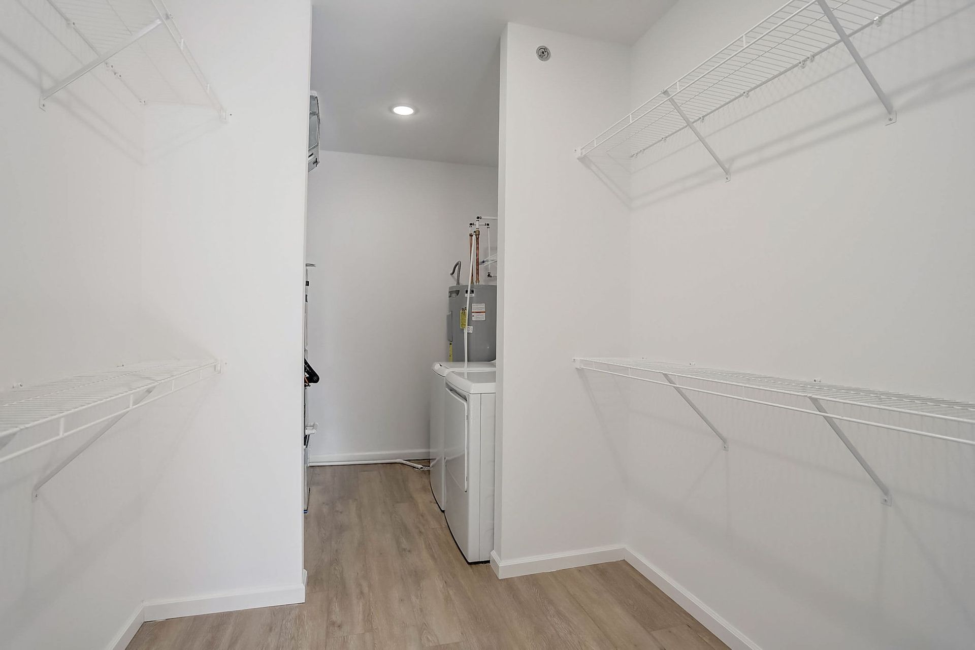 Bright white walk-in closet with wire shelves on both sides and wood flooring, opening to a small vanity area.
