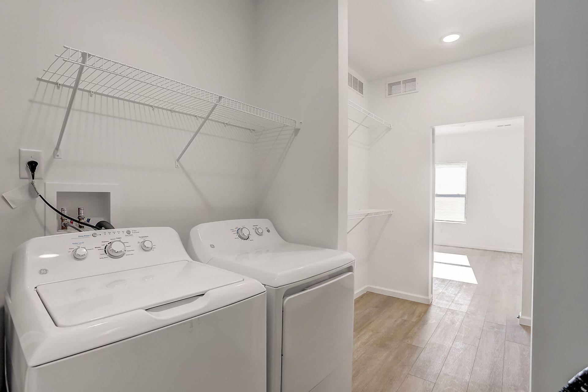 Laundry room with a white washer and dryer under wall-mounted shelves and a doorway to a bright hall