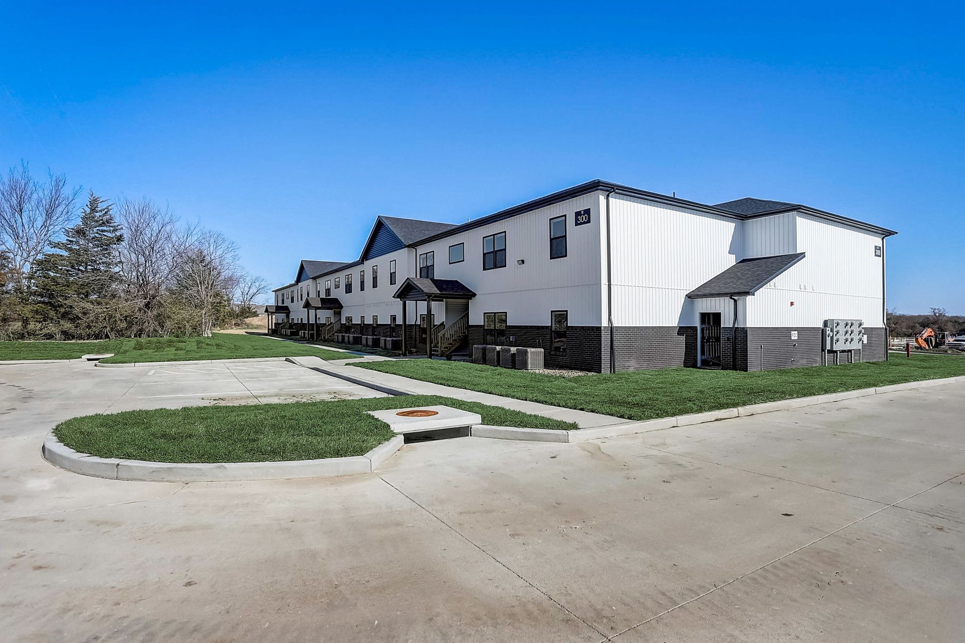 White apartment building with black trim and a paved driveway under a clear blue sky