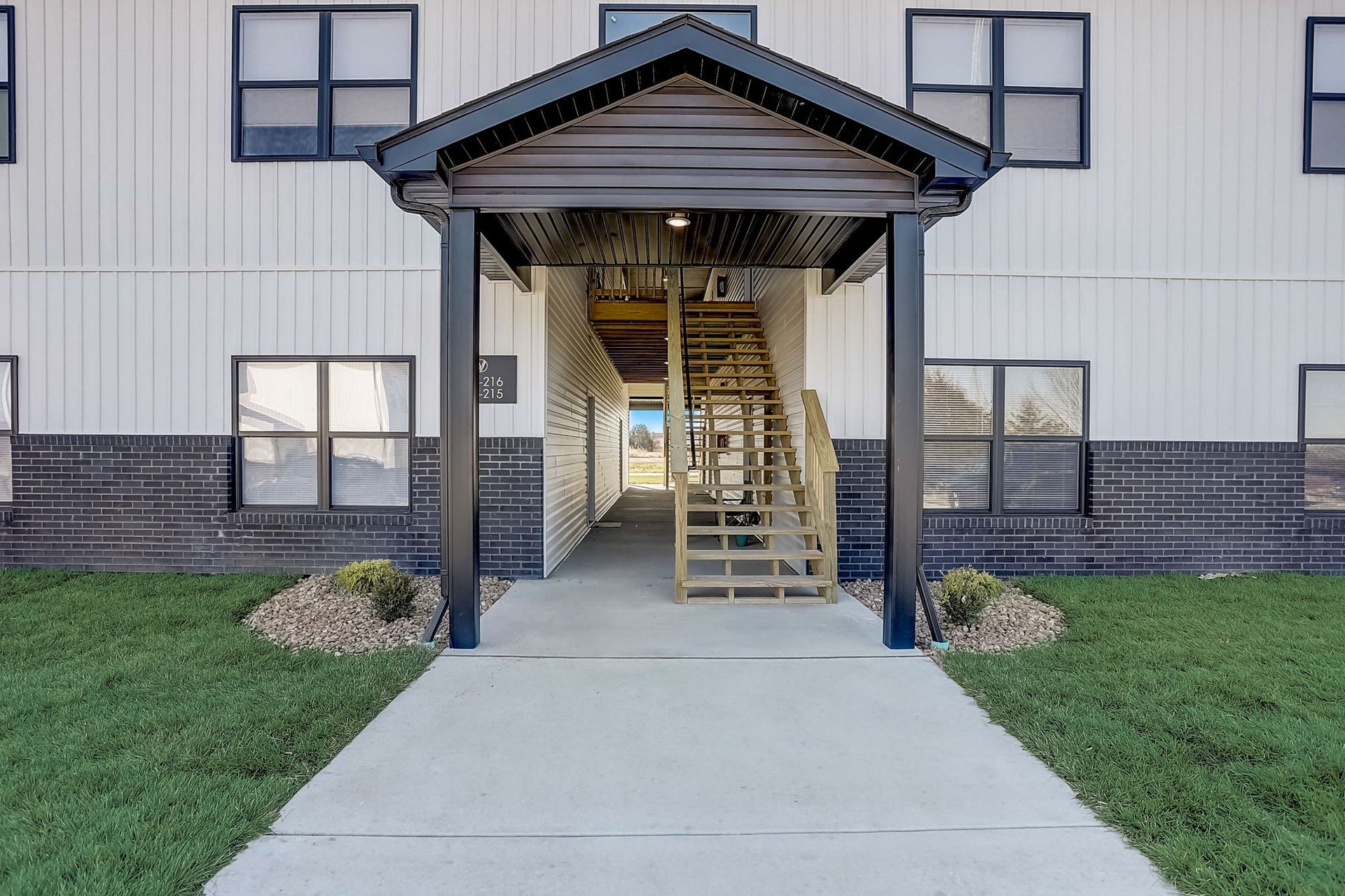 Apartment building entrance with covered walkway, concrete path, and stairs inside a white-and-gray facade