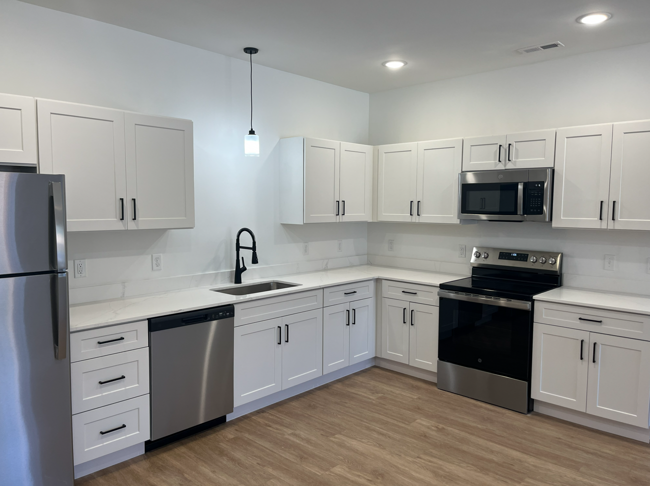 Bright modern kitchen with white cabinets, stainless appliances, and wood flooring