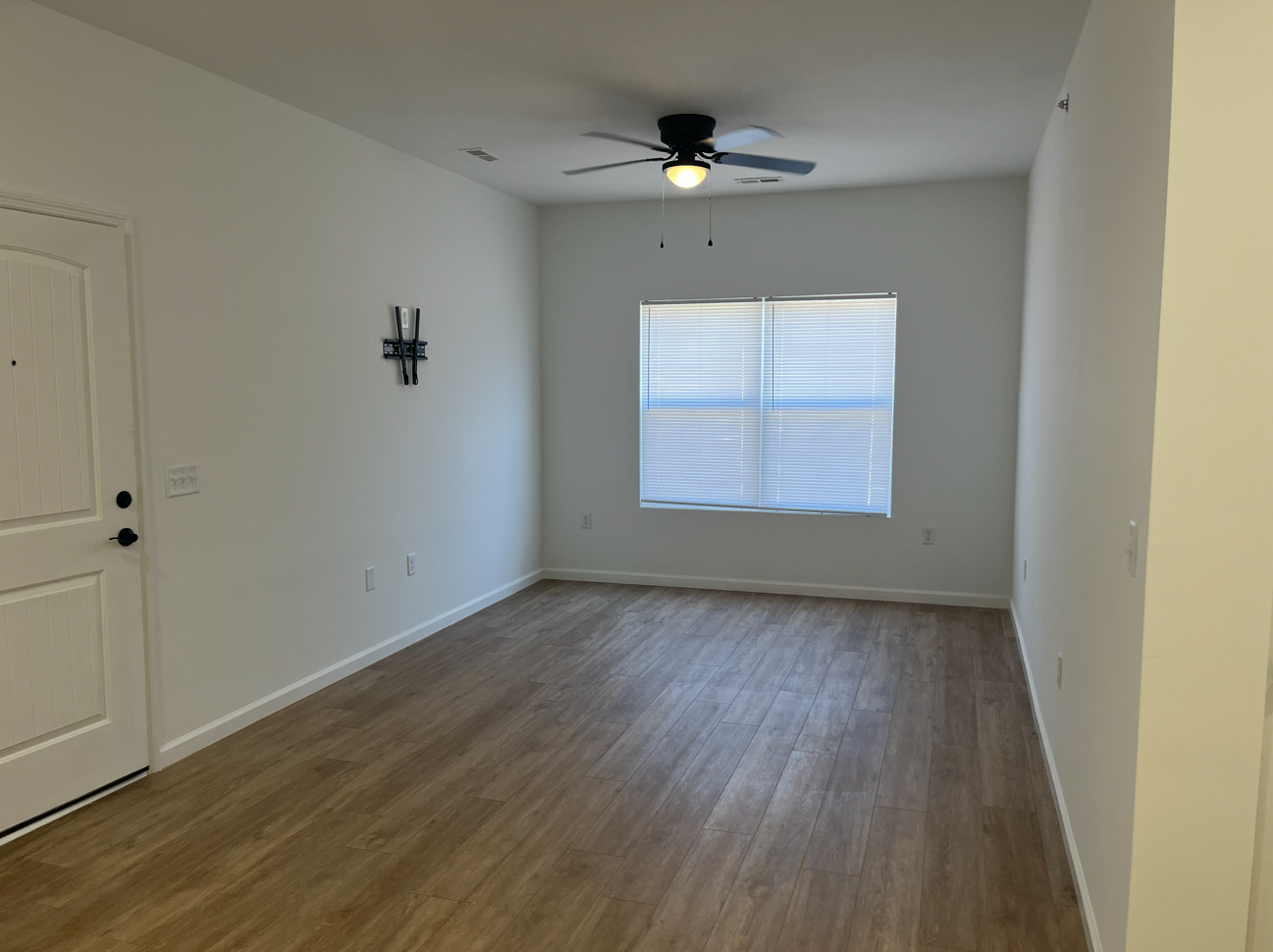 Empty unfurnished room with wood flooring, white walls, a ceiling fan, and a window with blinds.
