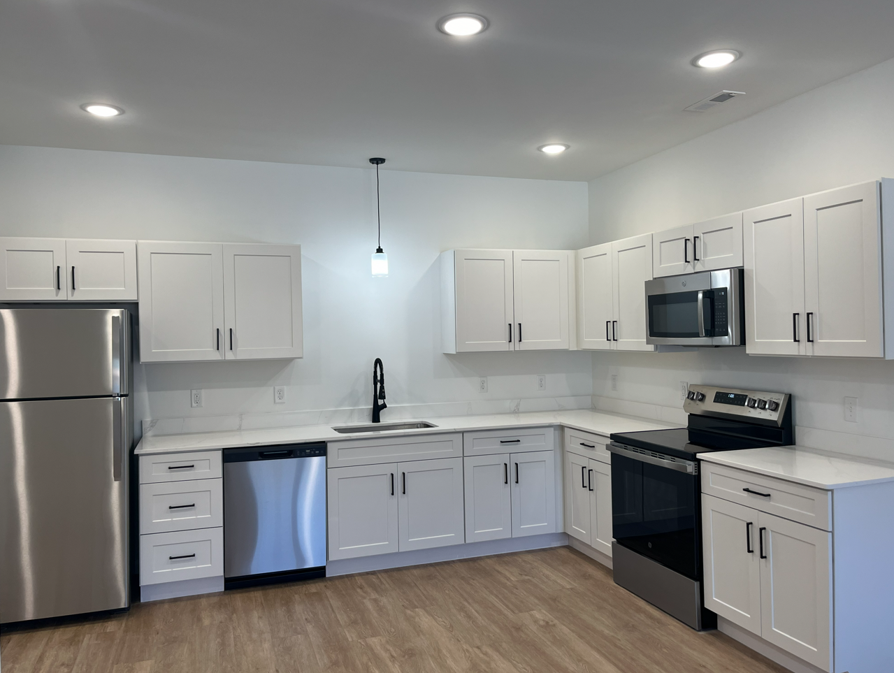 Bright white kitchen with stainless steel appliances, black countertops, and recessed ceiling lights.