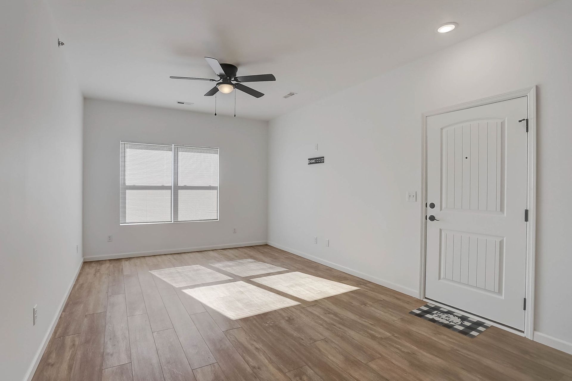Empty white room with wood floors, ceiling fan, window, and a closed door