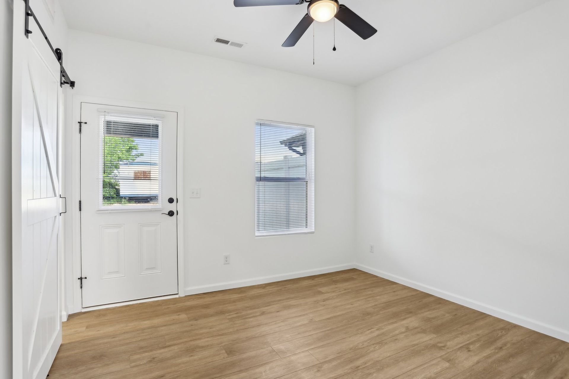 Empty white bedroom with wood-look floor, ceiling fan, window, and white door to outside
