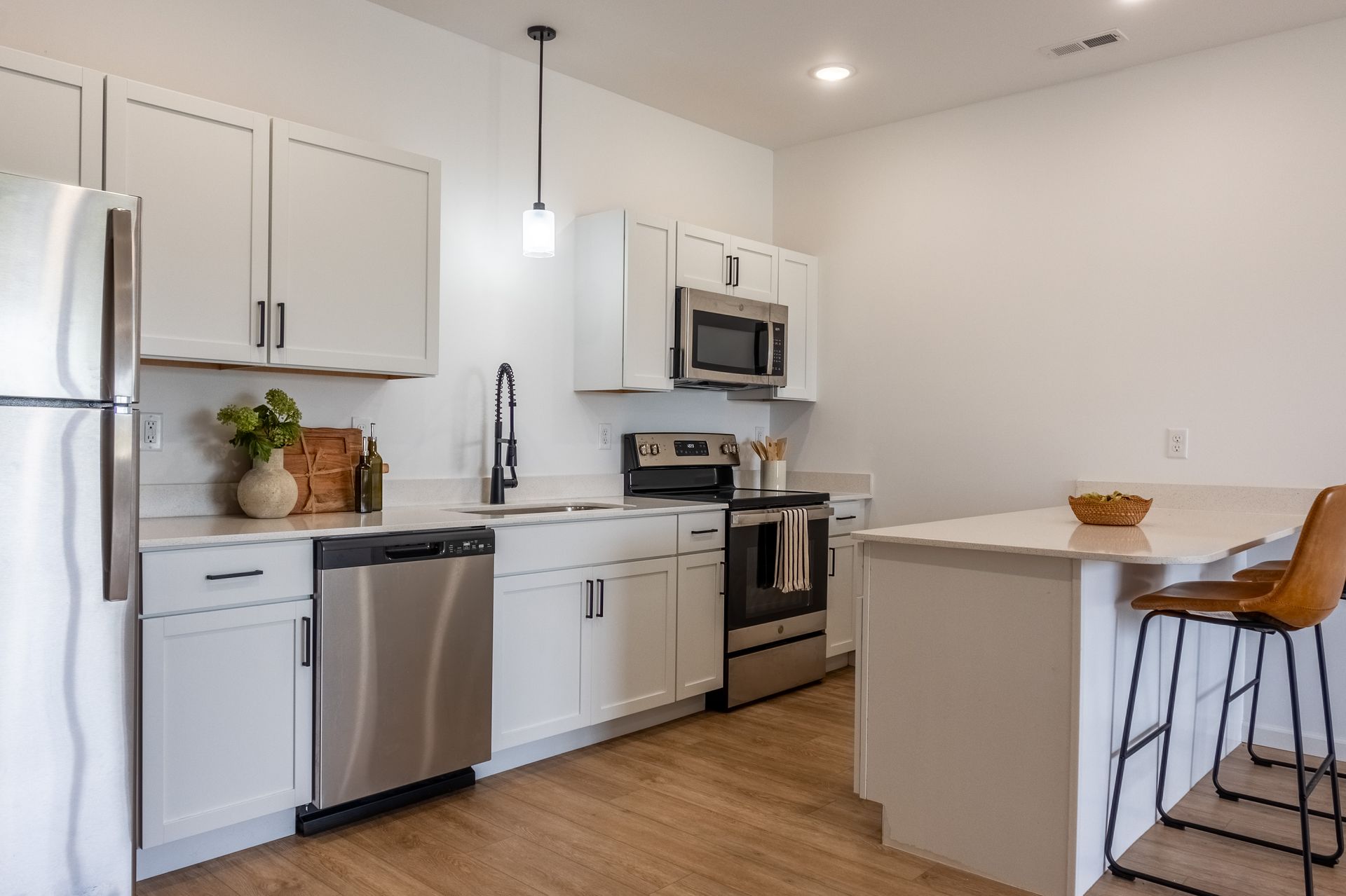 Modern white kitchen with stainless steel appliances, wood floor, and a breakfast bar with two stools