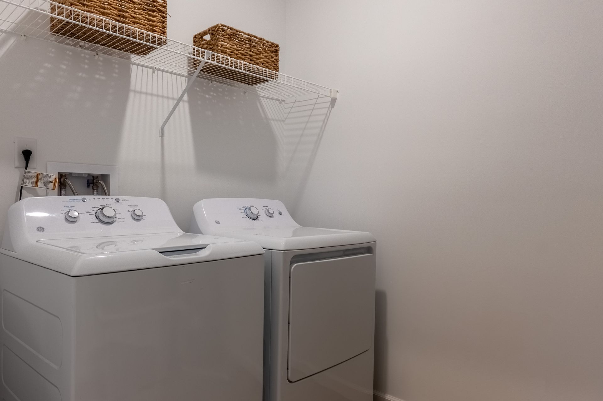 Laundry room with a white washer and dryer beneath wall-mounted wicker baskets
