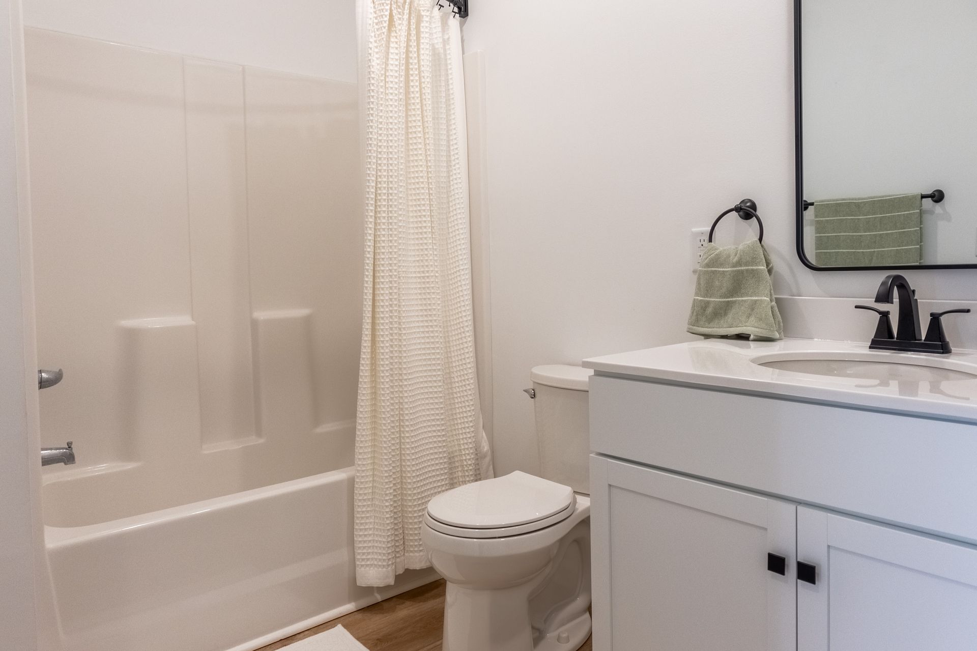 Small bathroom with a tub, shower curtain, toilet, and vanity with sink and mirror.
