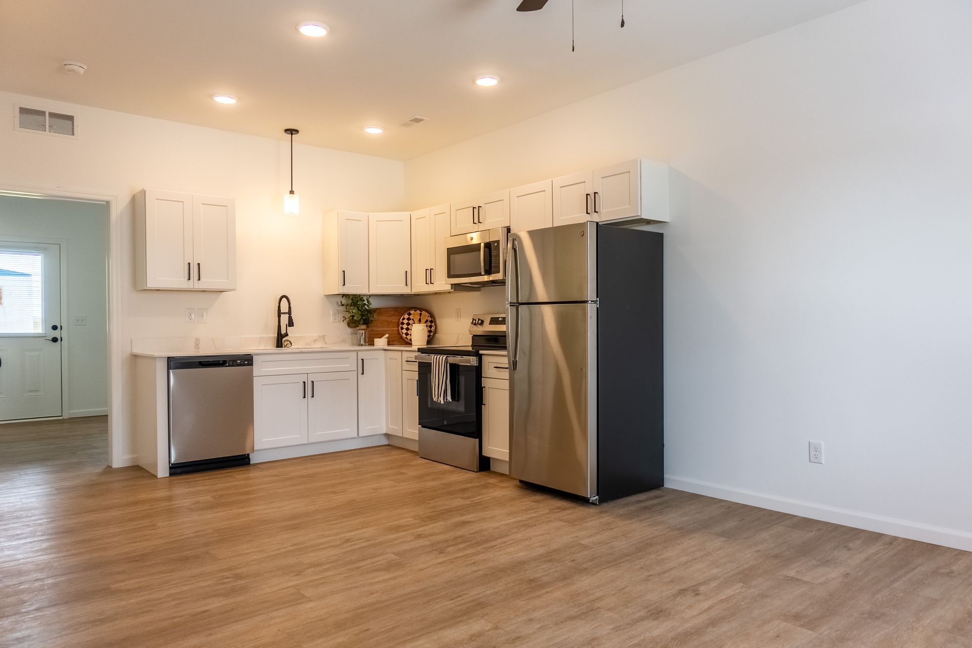 Bright empty kitchen with white cabinets, stainless steel appliances, and wood floors