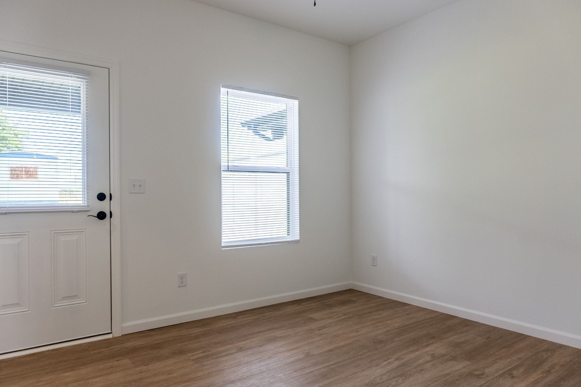 Empty white room with wood flooring, a door, and a narrow window letting in sunlight