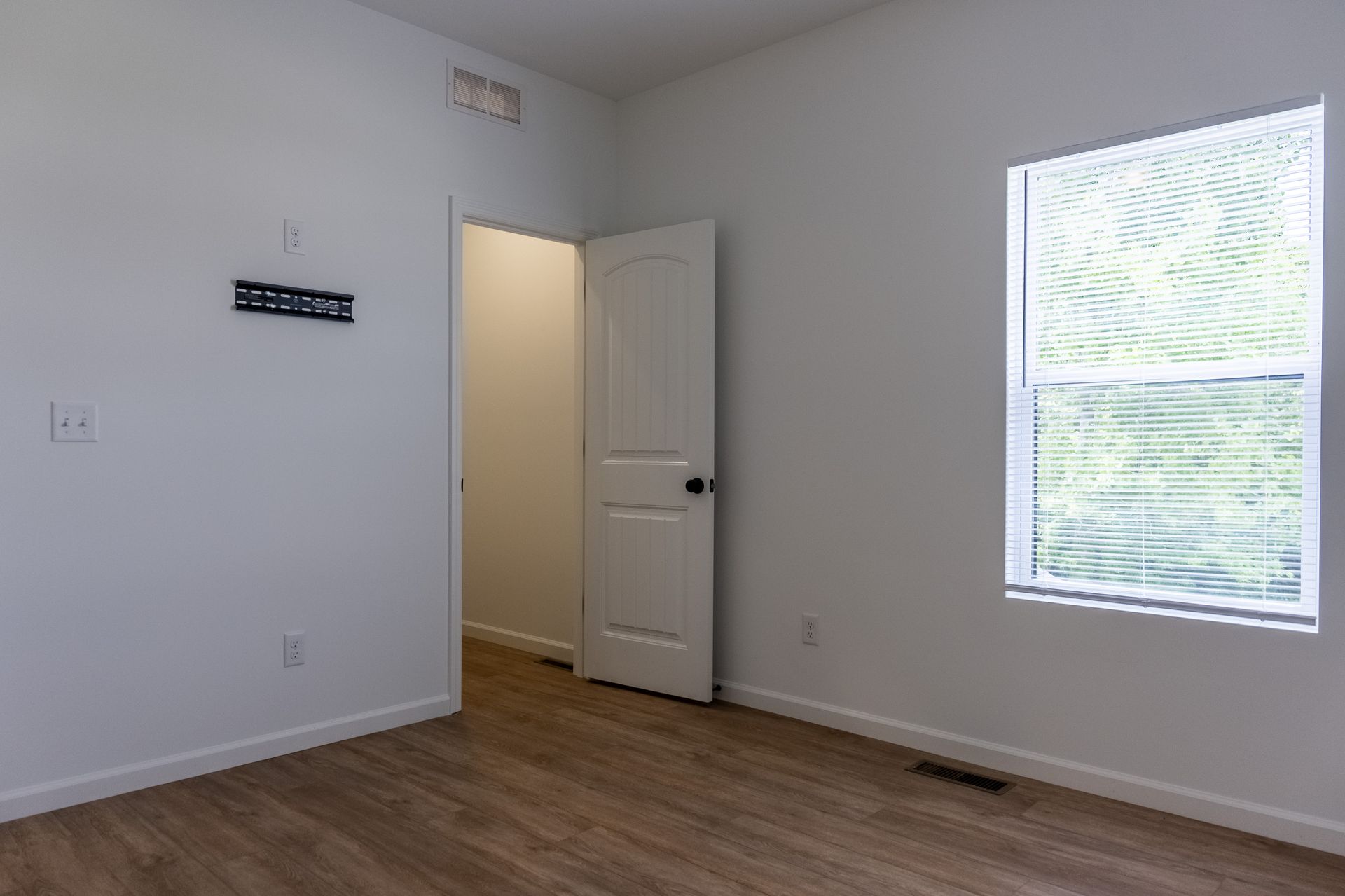 Empty white room with wood floor, open door, and a sunlit window.