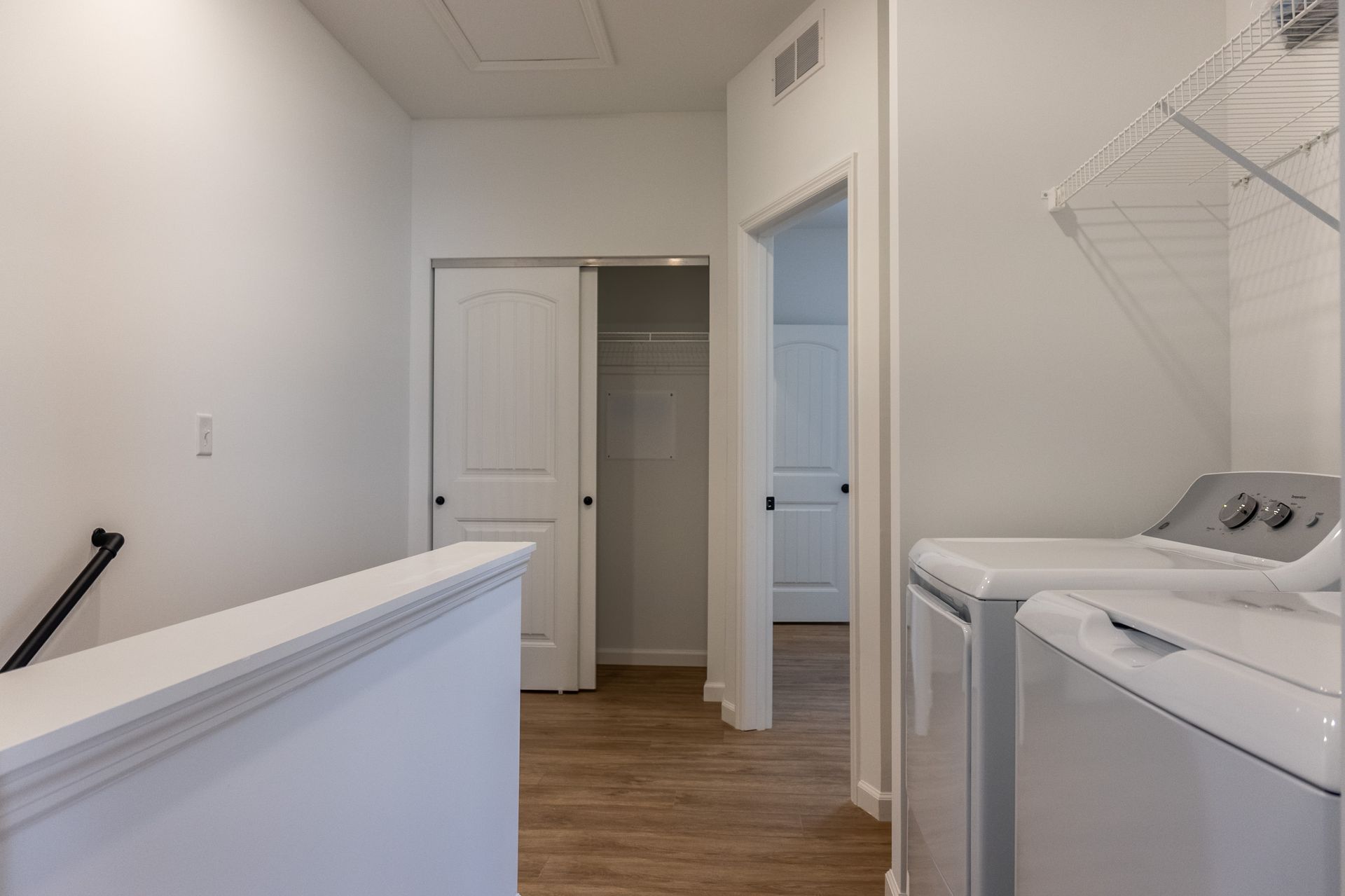 Laundry room with washer and dryer, white walls, and wood flooring; open door to a hallway.