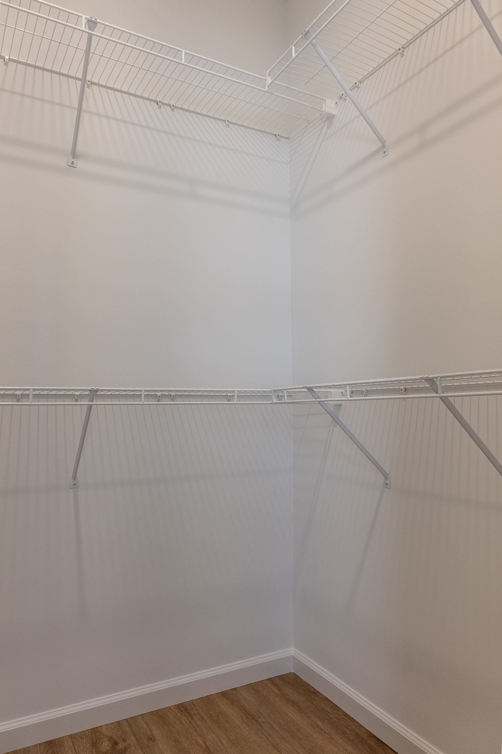 Empty white walk-in closet with wire shelving and light wood floor