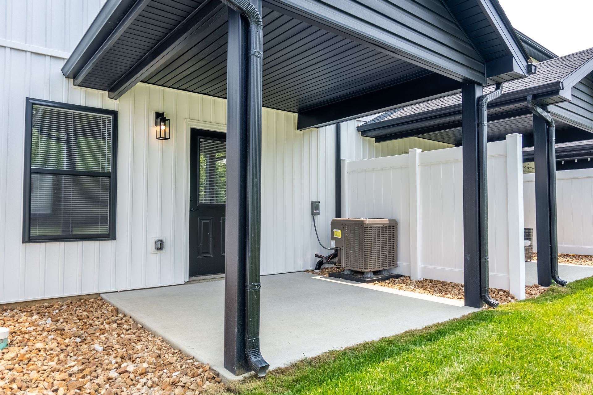 Covered patio with black posts, concrete floor, and outdoor AC unit beside a white house.