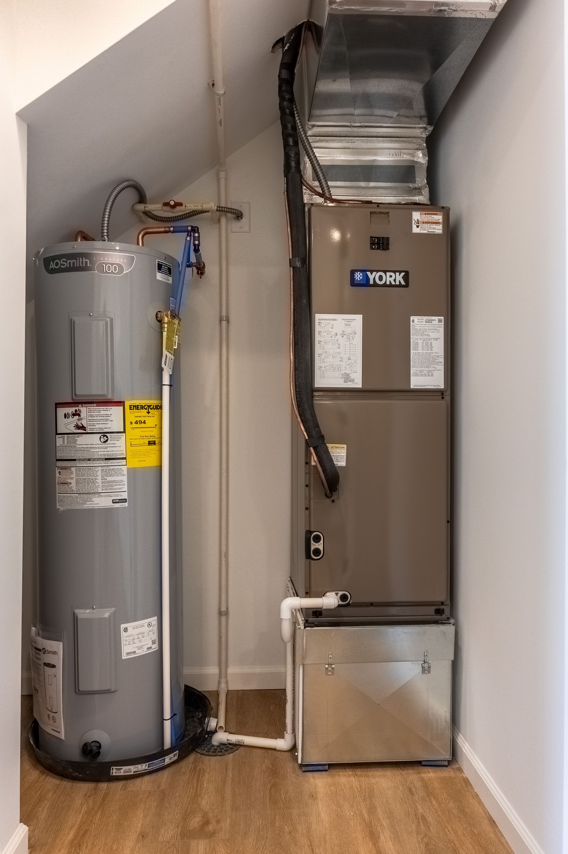 HVAC air handler and water heater in a narrow utility closet with exposed piping and ductwork