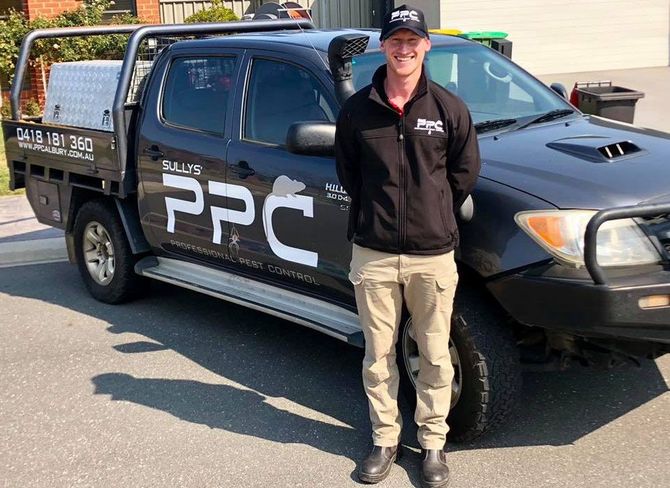 A smiling technician in a uniform standing beside a black PPC-branded work truck in a parking lot.