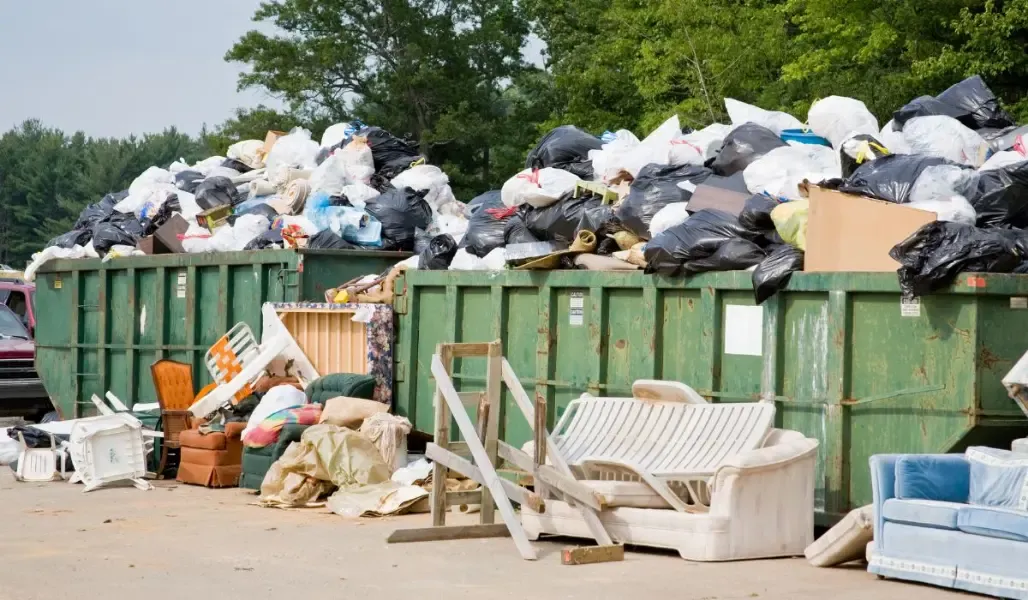 A large pile of garbage is sitting in front of a dumpster.