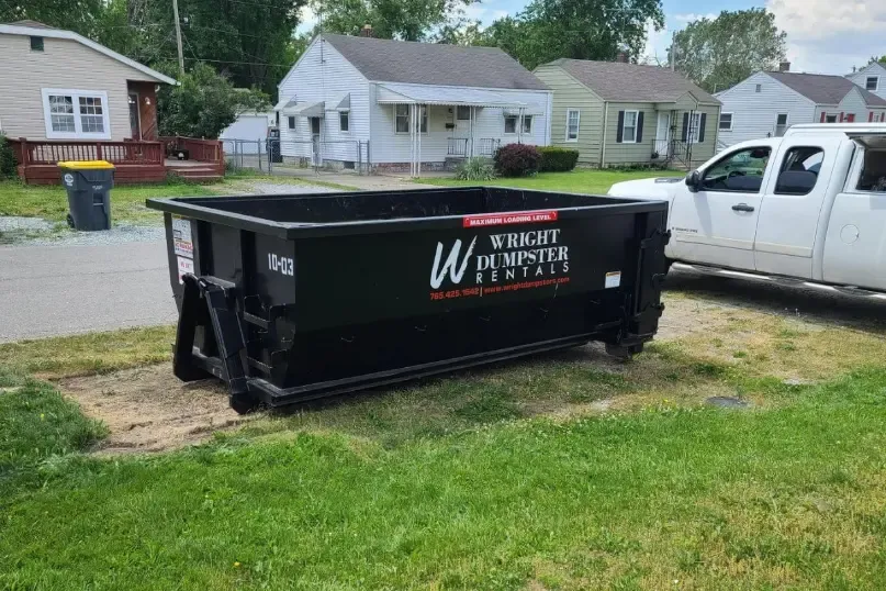 A dumpster is sitting in the grass next to a truck.