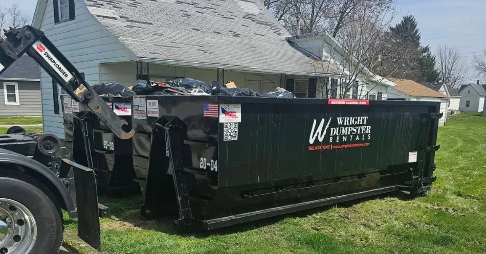 A dumpster is sitting in the grass in front of a house.