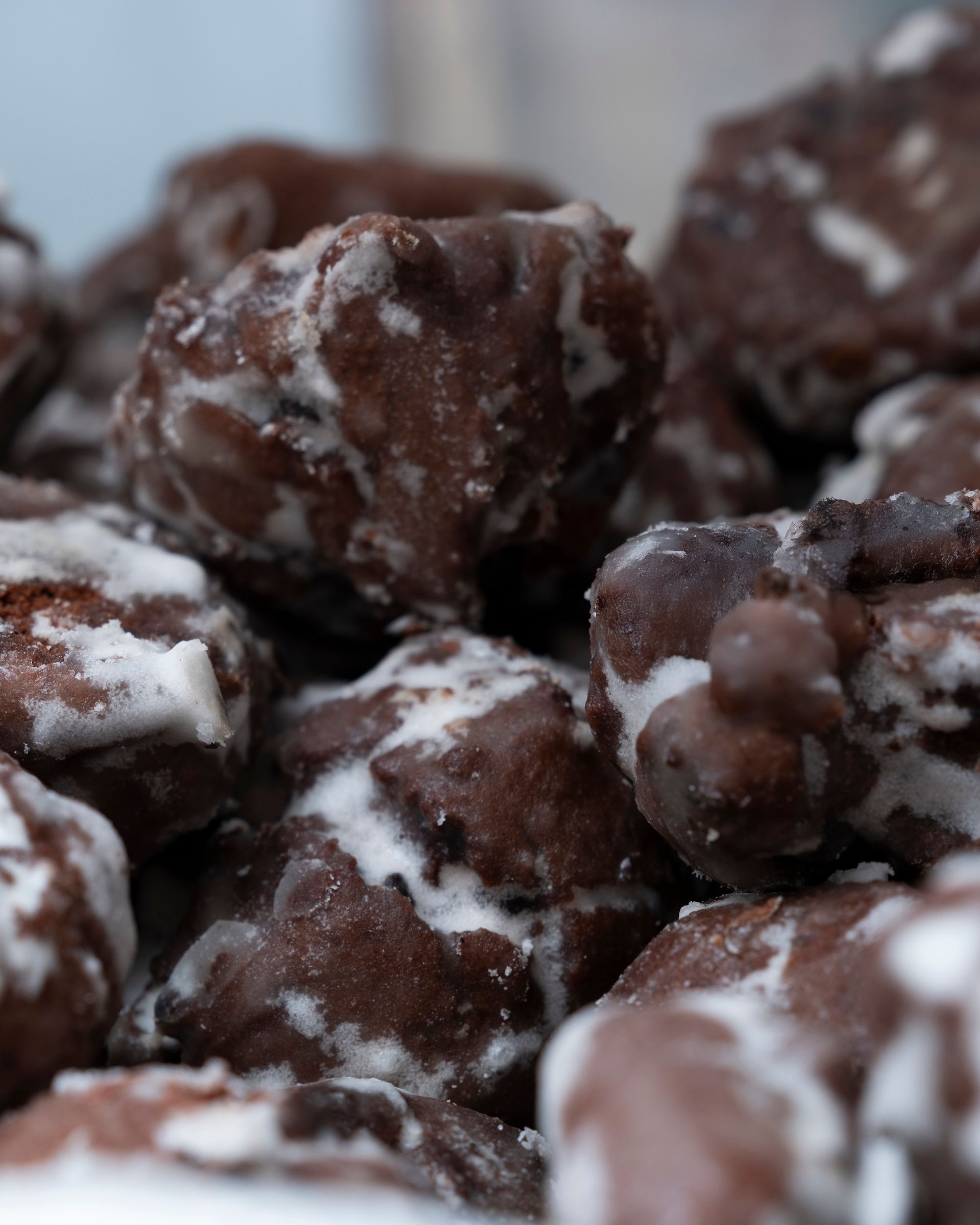 Frittelle glassate al cioccolato, ammucchiate una vicino all'altra, ricoperte di glassa bianca.
