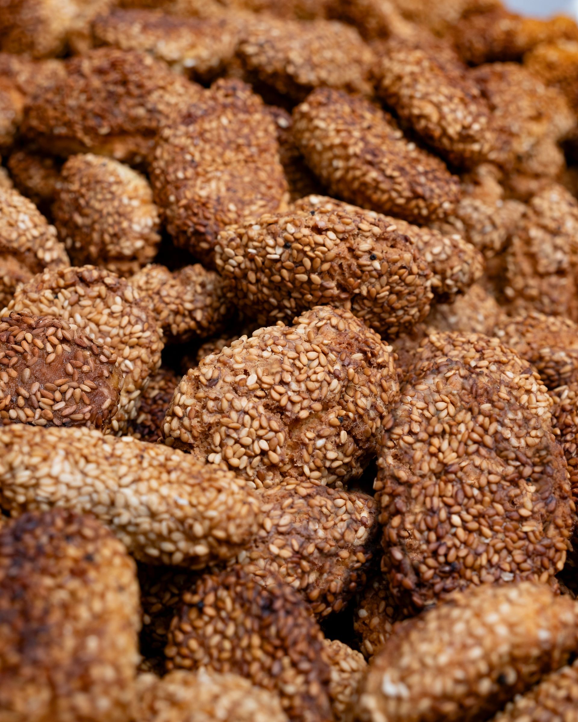 Primo piano di una pila di biscotti ricoperti di sesamo, marroni e dorati, disposti in un mucchio strutturato.