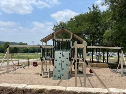 A playground with a climbing wall and swings in a park.