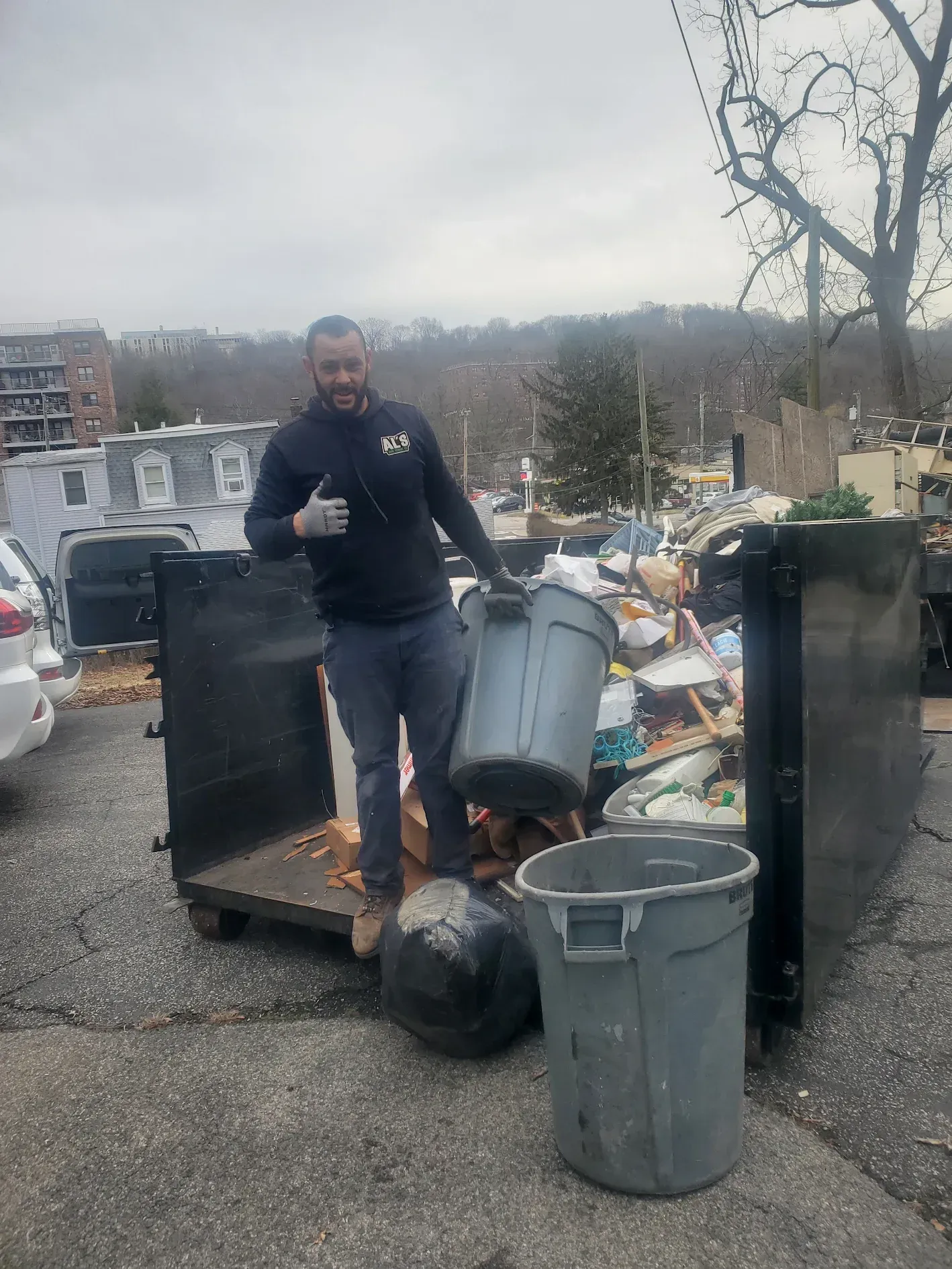 A man is standing in front of a dumpster full of trash.